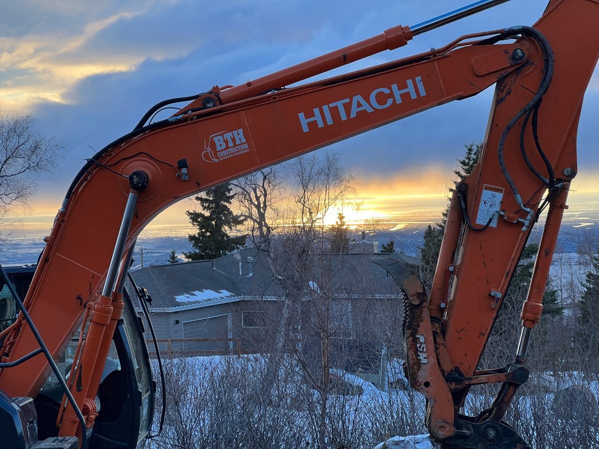BTH Construction Hitachi excavator arm framing winter sunset over Anchorage and Cook Inlet, Alaska