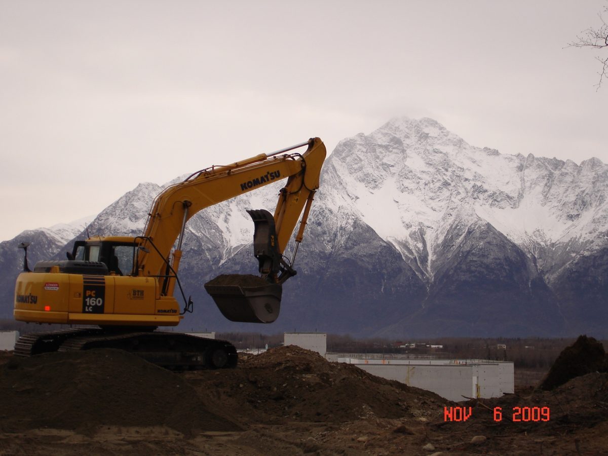BTH Construction excavator with snow-capped Chugach mountains in background, Anchorage Alaska