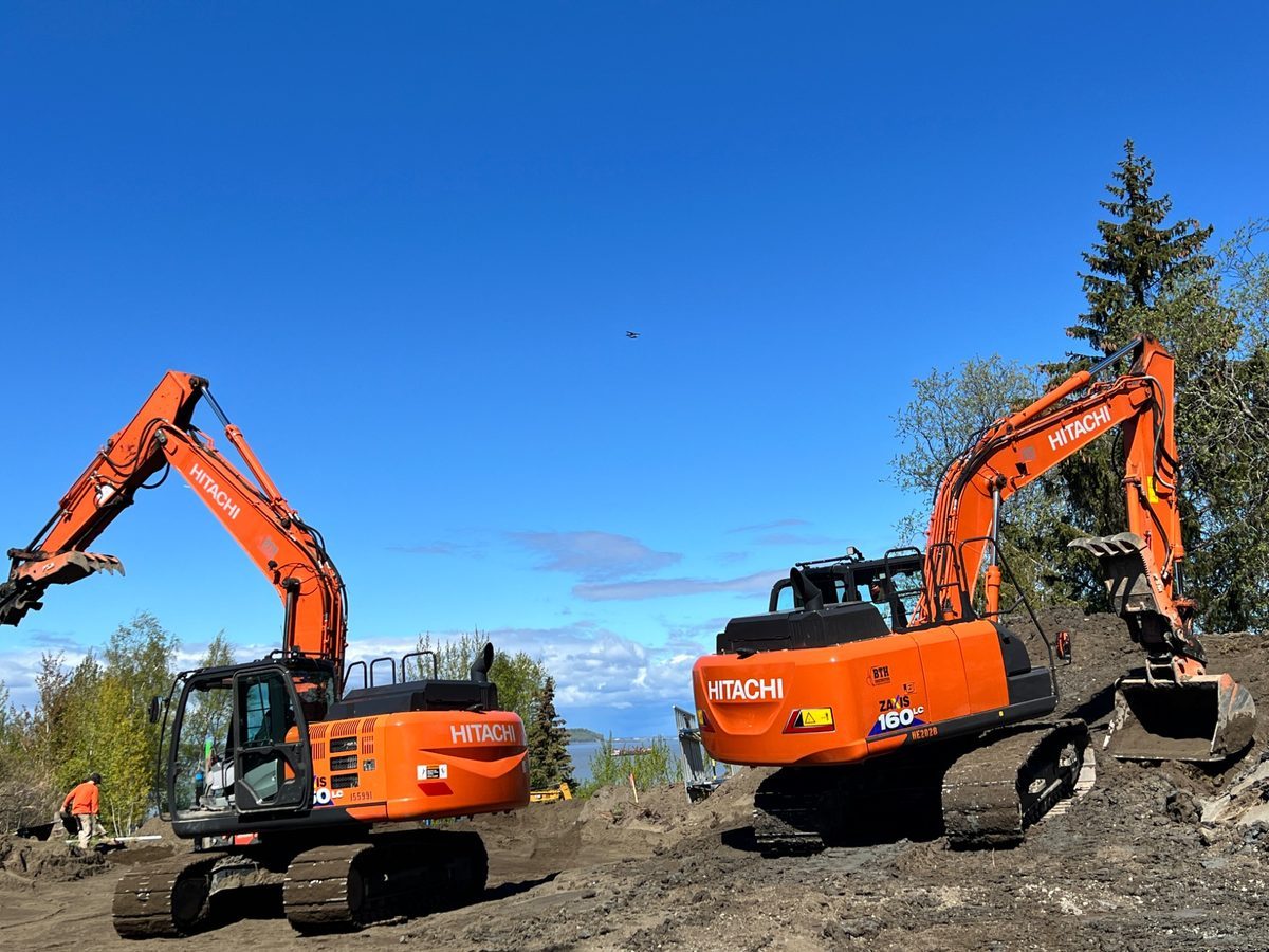 Two BTH Construction Hitachi ZAXIS 160LC excavators on site prep job with Cook Inlet in background, Anchorage Alaska